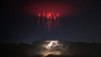 a cluster of what look like red lightning bolts appear in the sky above a storm cloud lit up by lightning